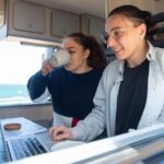 A joyful couple works on a laptop in a cozy camper van with ocean views. - Photo by Kampus Production on Pexels
