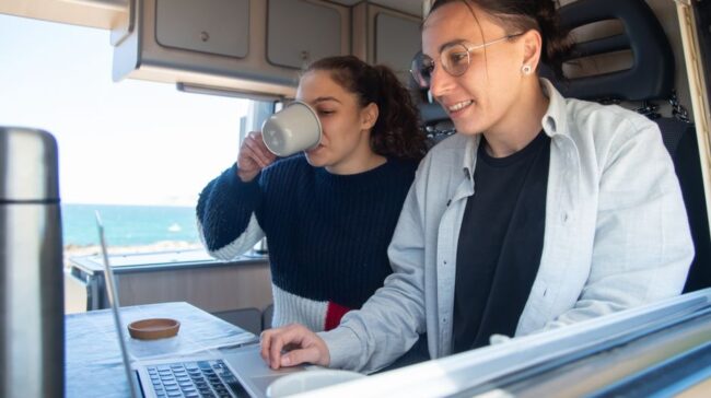 A joyful couple works on a laptop in a cozy camper van with ocean views. - Photo by Kampus Production on Pexels