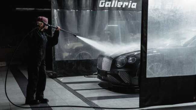 A woman power washing a luxury car in an indoor garage setting, showcasing car wash service. - Photo by Tima Miroshnichenko on Pexels