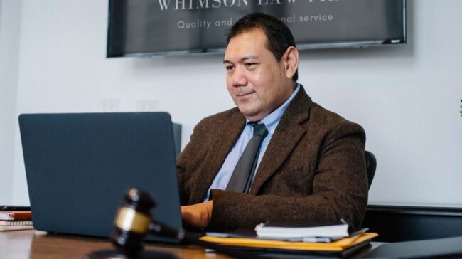 Experienced middle aged ethnic happy male working with netbook at table with judge hammer - Photo by Sora Shimazaki on Pexels
