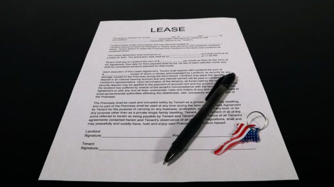 Lease agreement document with pen and American flag keychain on a black table. - Photo by Artful Homes on Pexels